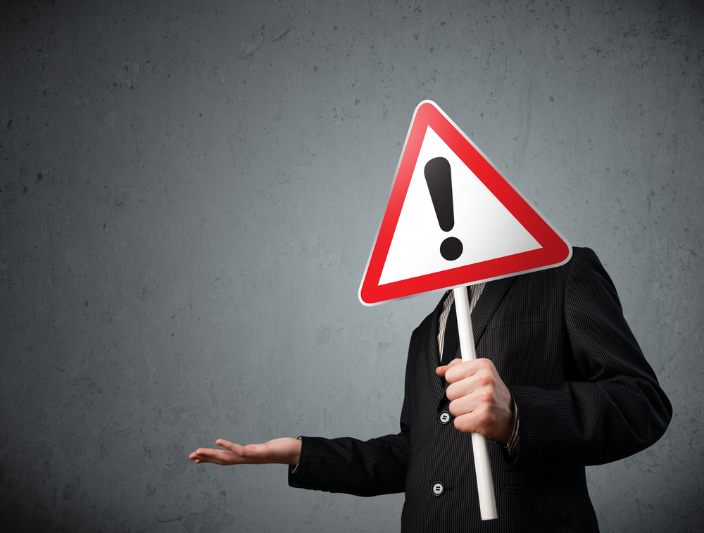 Businessman holding a red traffic triangle warning sign in front of his head