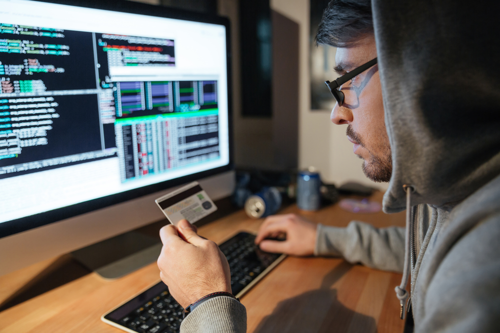 Concentrated young hacker in glasses stealing money from different credit cards sitting in dark room