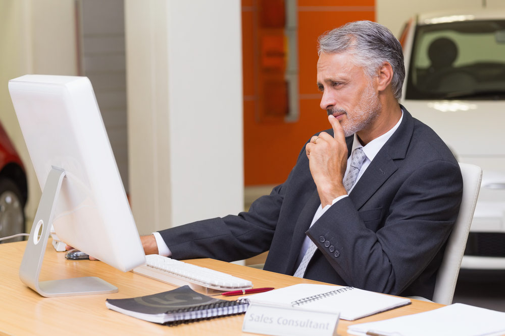 Focused businessman using his laptop at new car showroom